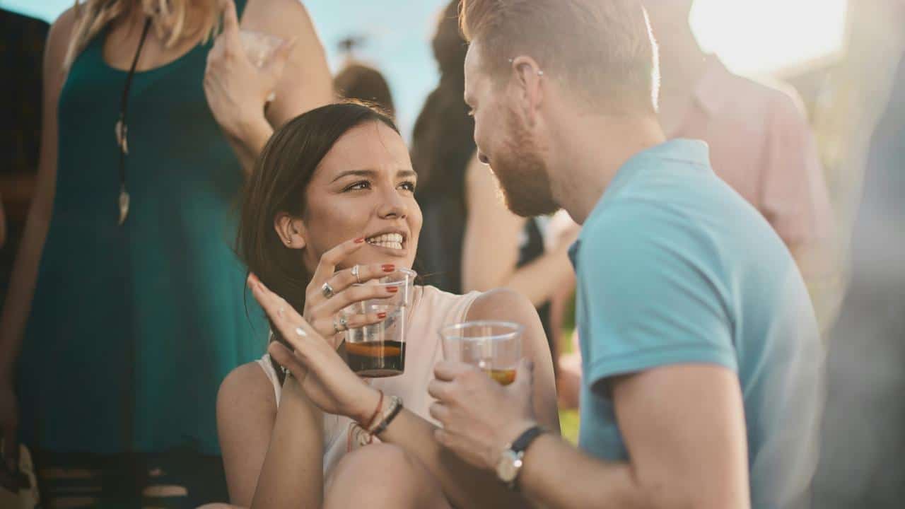 A woman and man smiling and talking while holding drinks at a social gathering.