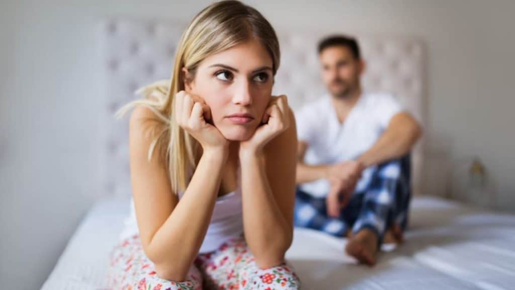 Couple sitting on bed looking distant