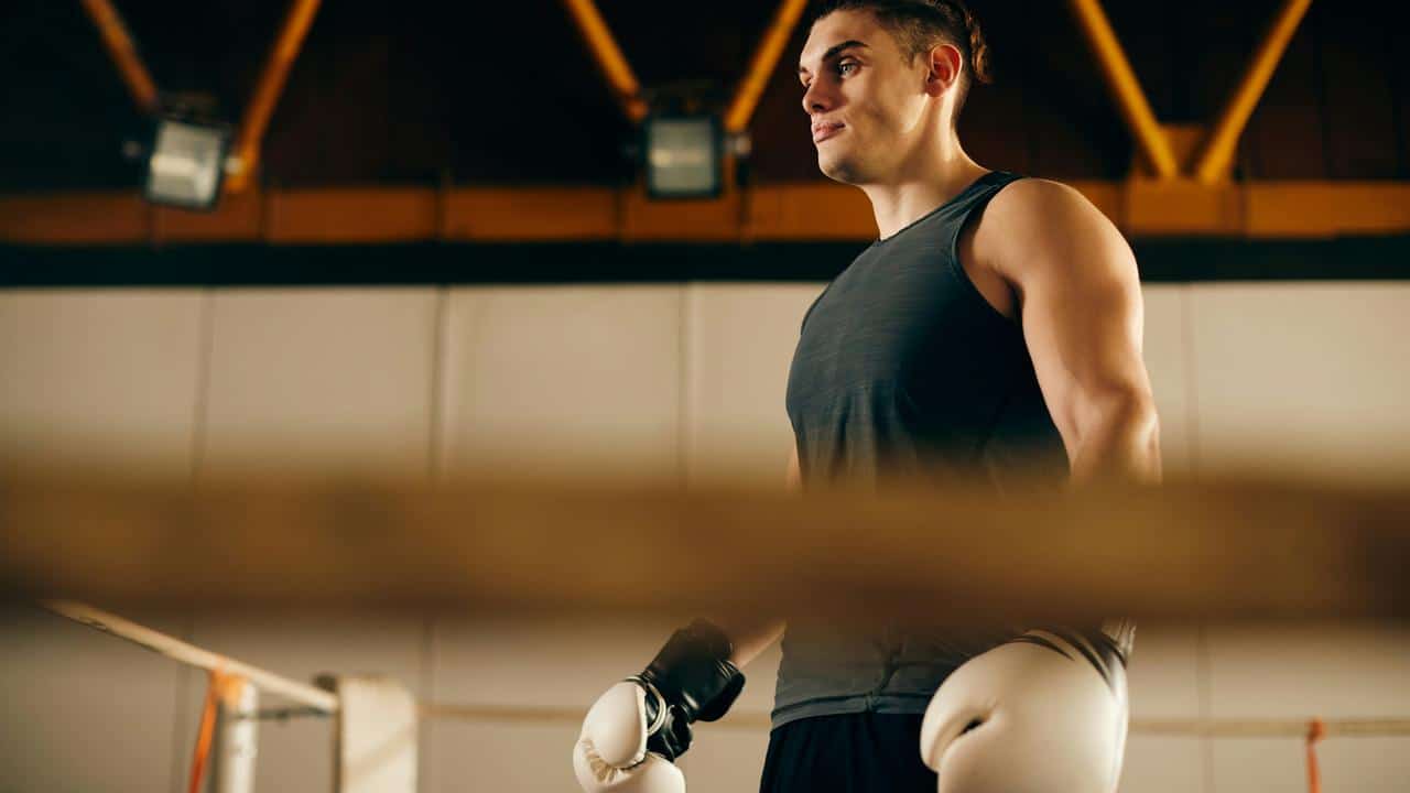 A man in a sleeveless shirt wearing boxing gloves inside a gym.
