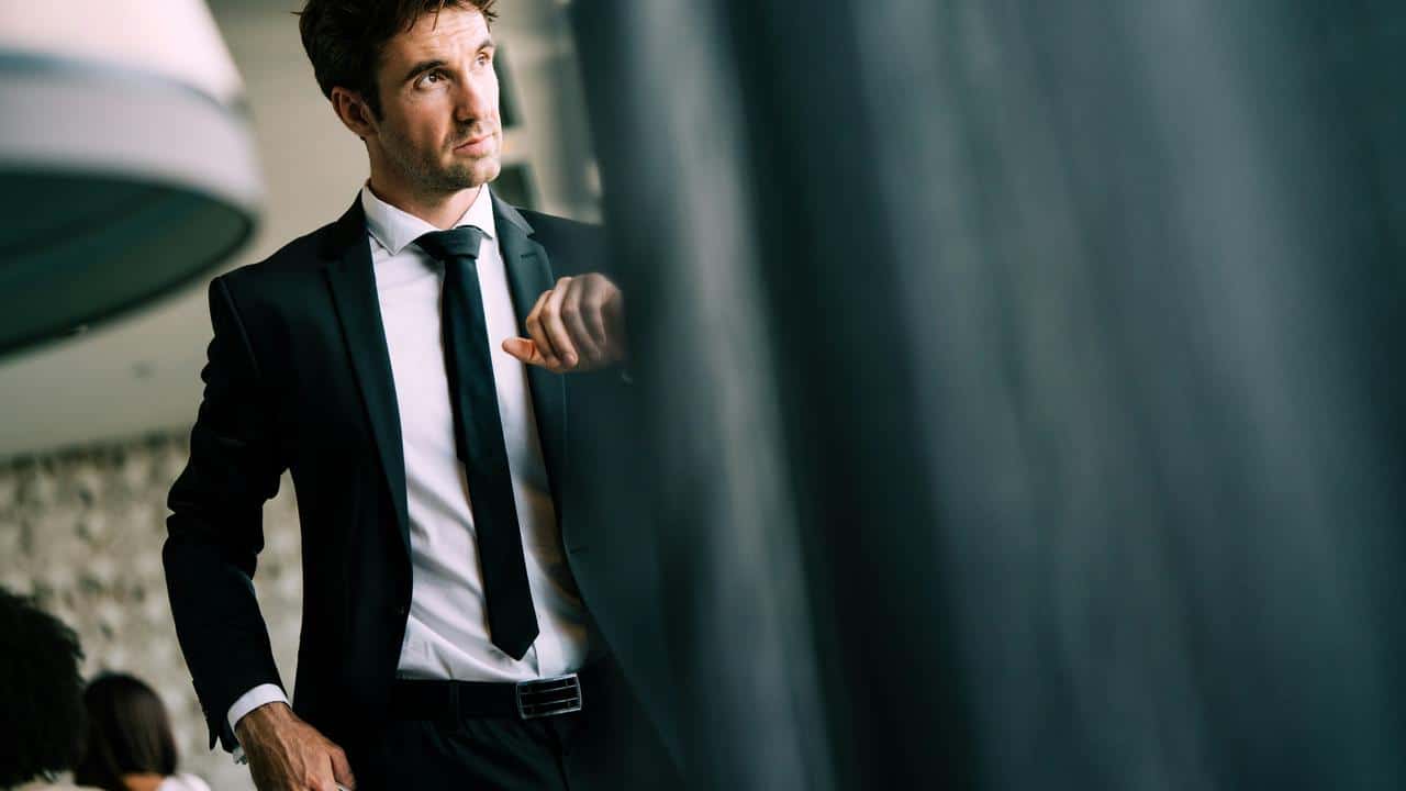 Man in a black tw0 piece suit with a white shirt and a black tie.