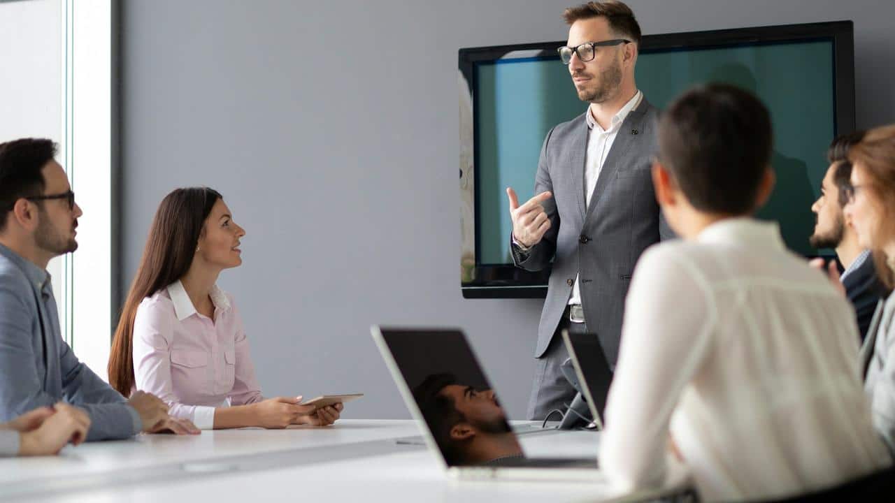A man in a suit giving a presentation to colleagues in a meeting room.