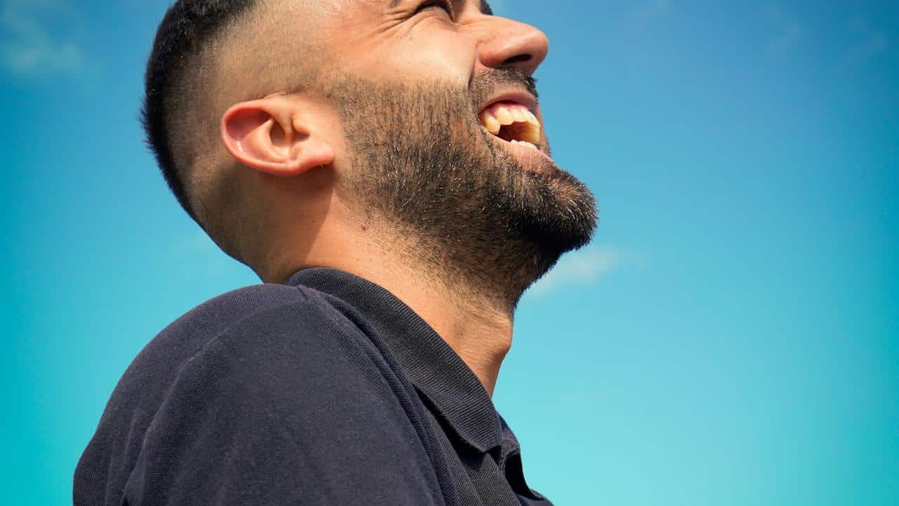 A man smiling and looking up against a clear blue sky.