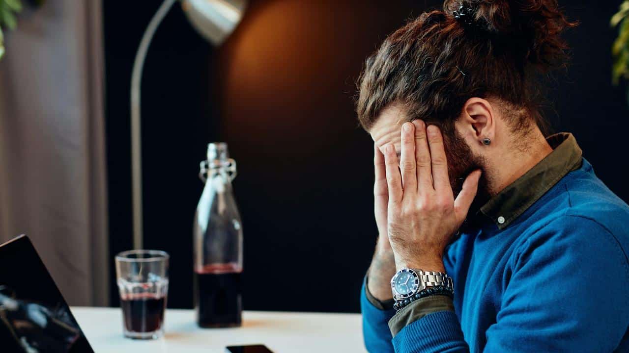 A man sitting at a desk with his face in his hands looking stressed.