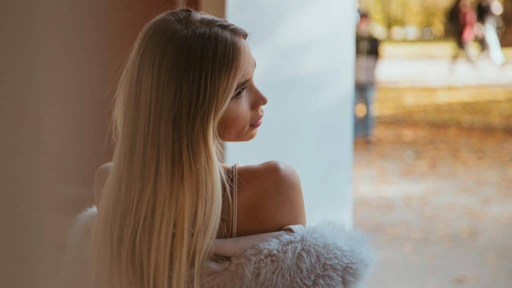 A woman with long blonde hair looking over her shoulder outdoors.