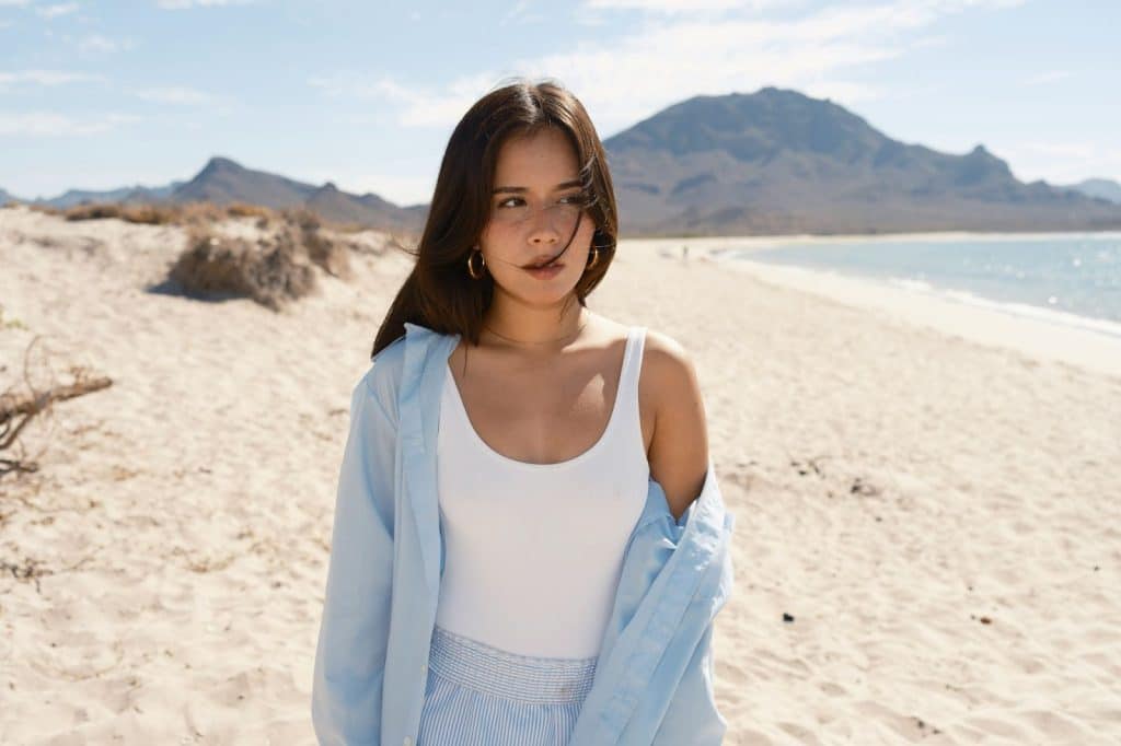 A woman standing on a sandy beach with mountains in the background.