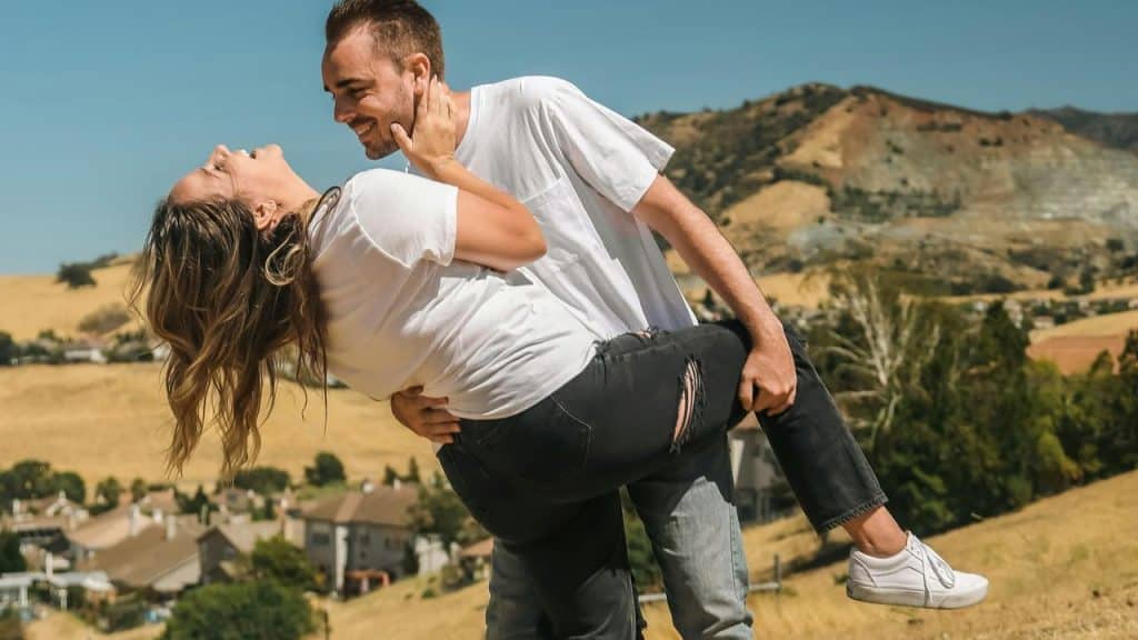 A man playfully holding a laughing woman outdoors.