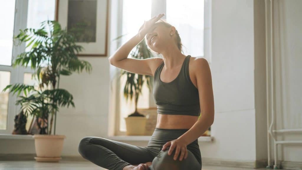 A woman in workout clothes sitting on the floor and laughing.