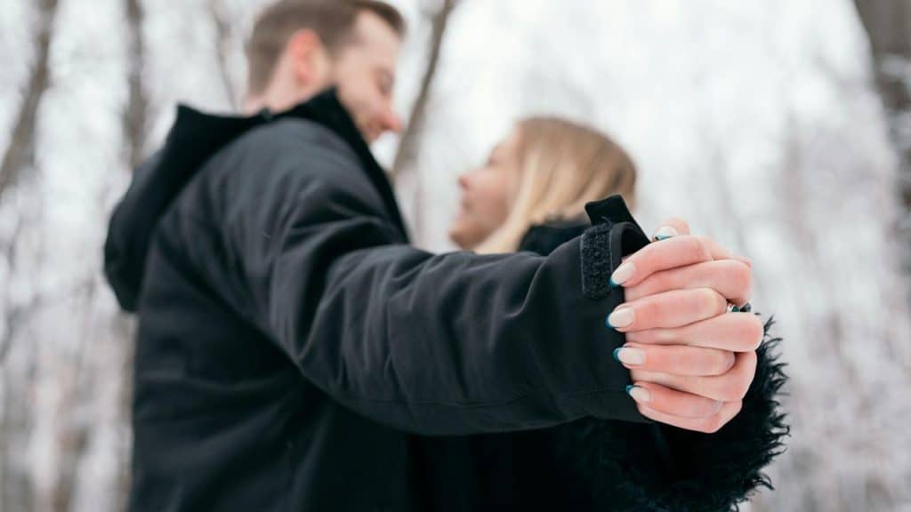 A couple holding hands while standing close together in a snowy forest.