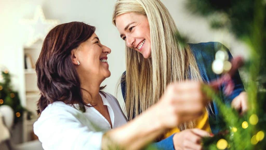 A couple smiling at each other while decorating a Christmas tree.