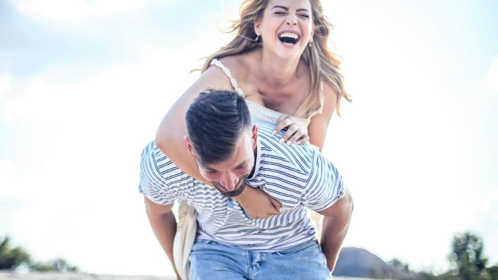 A laughing woman riding on a man's back during a piggyback ride outdoors.