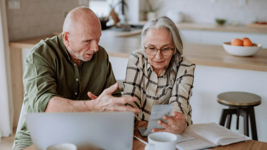 An older couple reviewing bills together at a kitchen table with a laptop.
