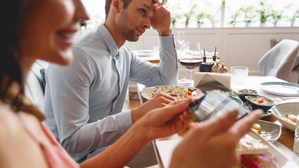 A smiling woman serving dinner and taking pictures of the food while her partner looks uninterested