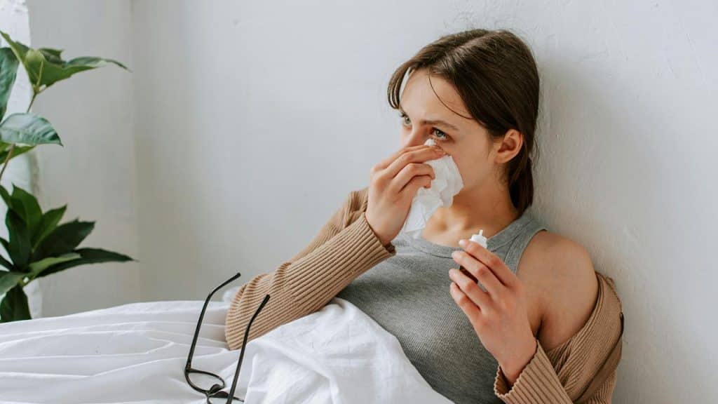 A woman sitting in bed wiping her tears with a tissue.