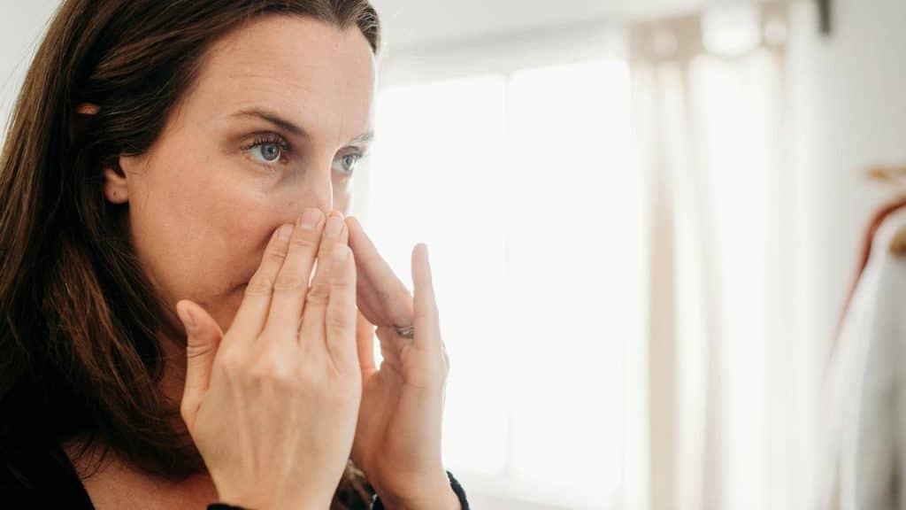 A woman touching her face and looking thoughtful.