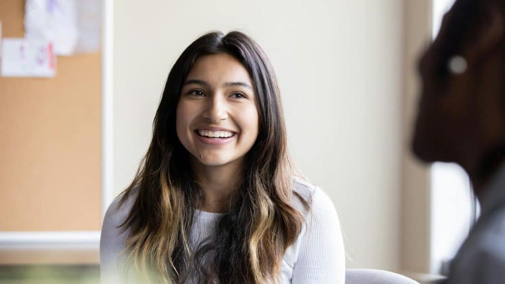 A young woman smiling while sitting indoors.