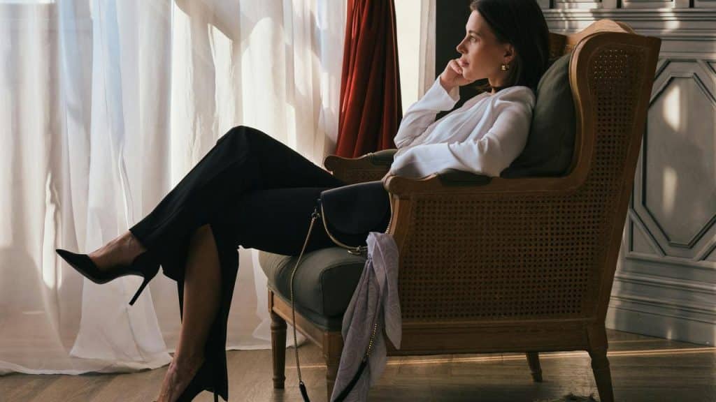 A woman sitting in a chair by the window looking thoughtful.