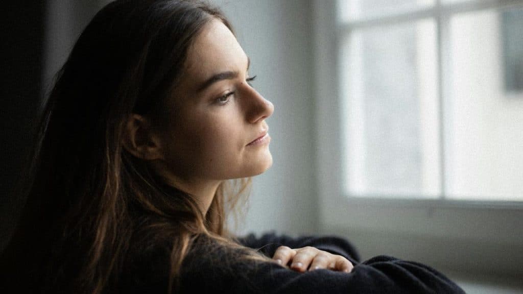 A woman resting her arms on a windowsill while gazing outside thoughtfully.