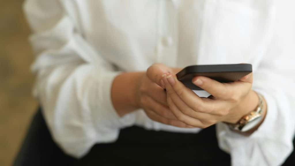 A person in a white shirt holding a smartphone with both hands.