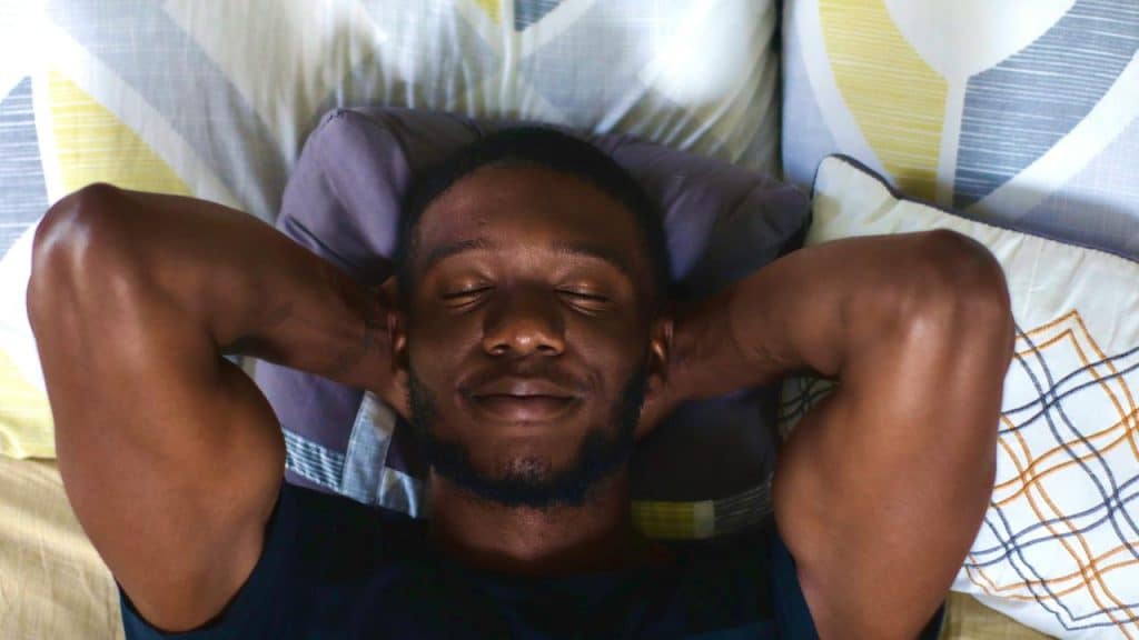 A man lying in bed with his hands behind his head.