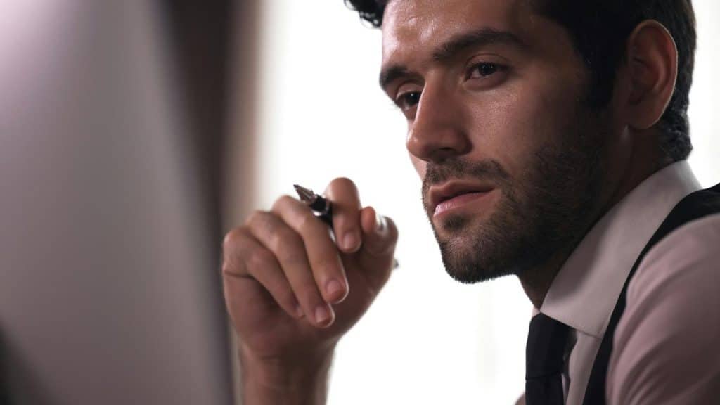 A man holding a pen and looking thoughtful.