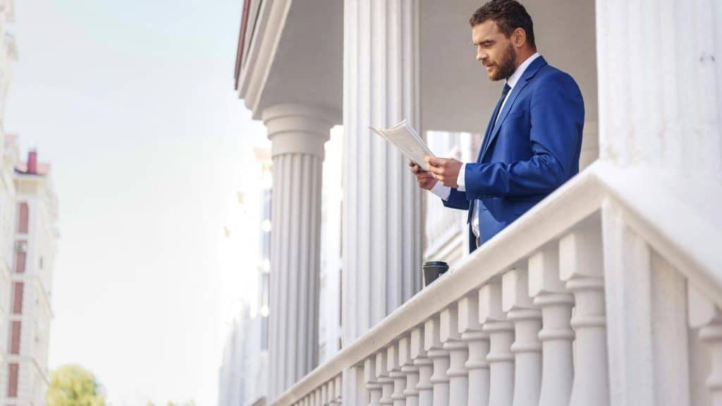 A man in a blue suit reading a newspaper outside.