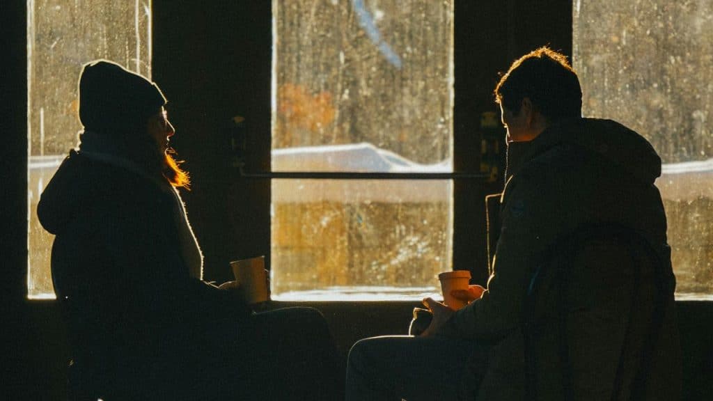 A man and woman sitting by a window with coffee cups.