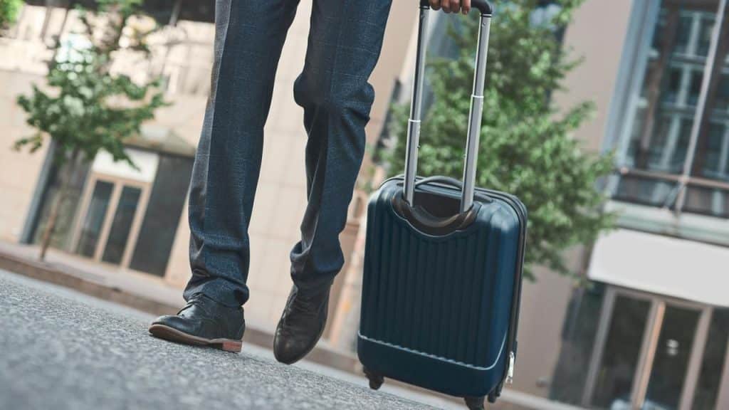 A man walking with a rolling suitcase.