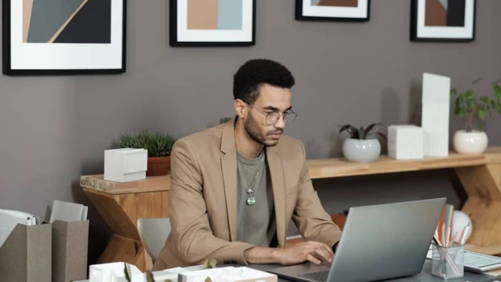 Man working on laptop with vision board in background