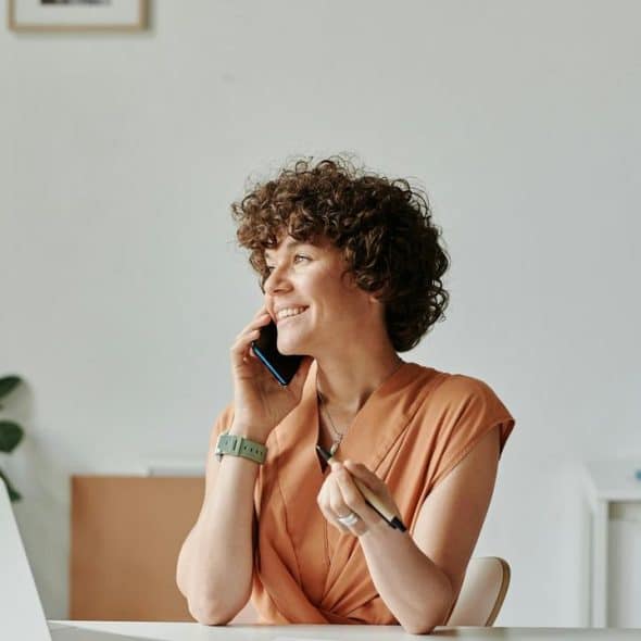 A woman smiling while talking on the phone at her desk.