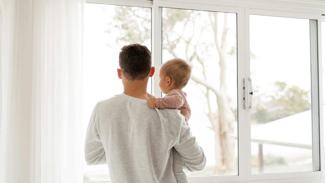 A man holding a baby while looking out a window.