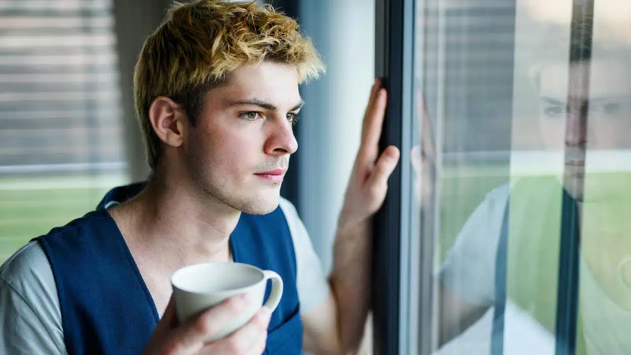 A man holding a cup while looking out a window.