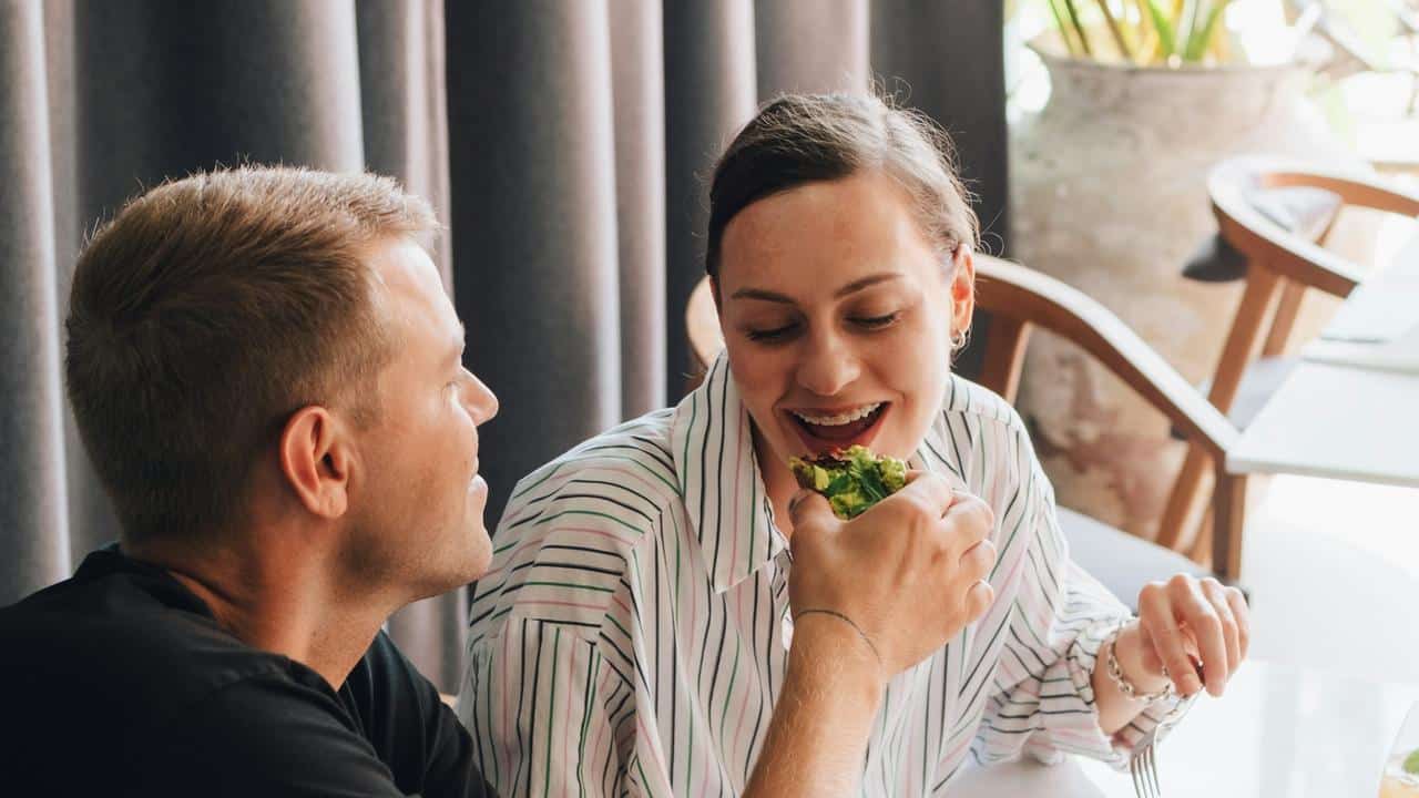 A man feeding a woman at a restaurant table.