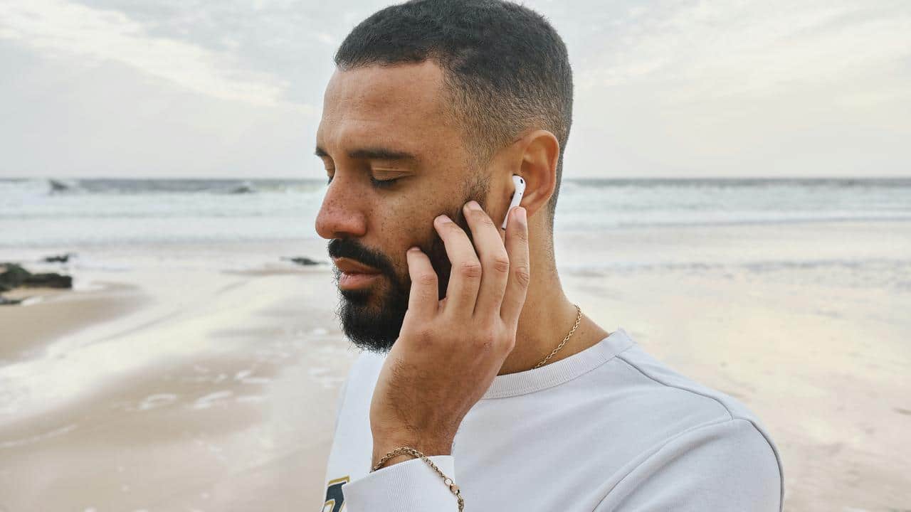 A man wearing wireless earbuds while standing on a beach.