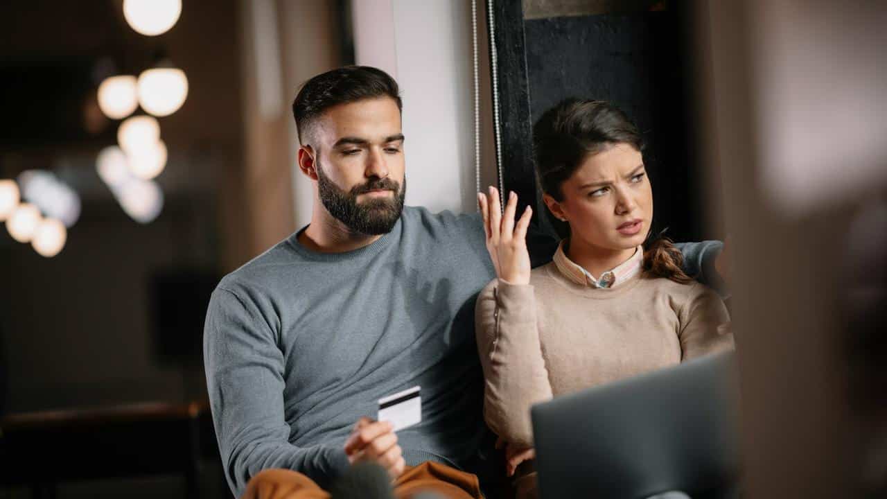 A couple sitting together with a laptop, looking frustrated during an online shopping session.