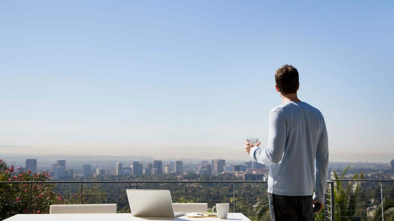A man holding a glass while looking at a city skyline from a balcony.