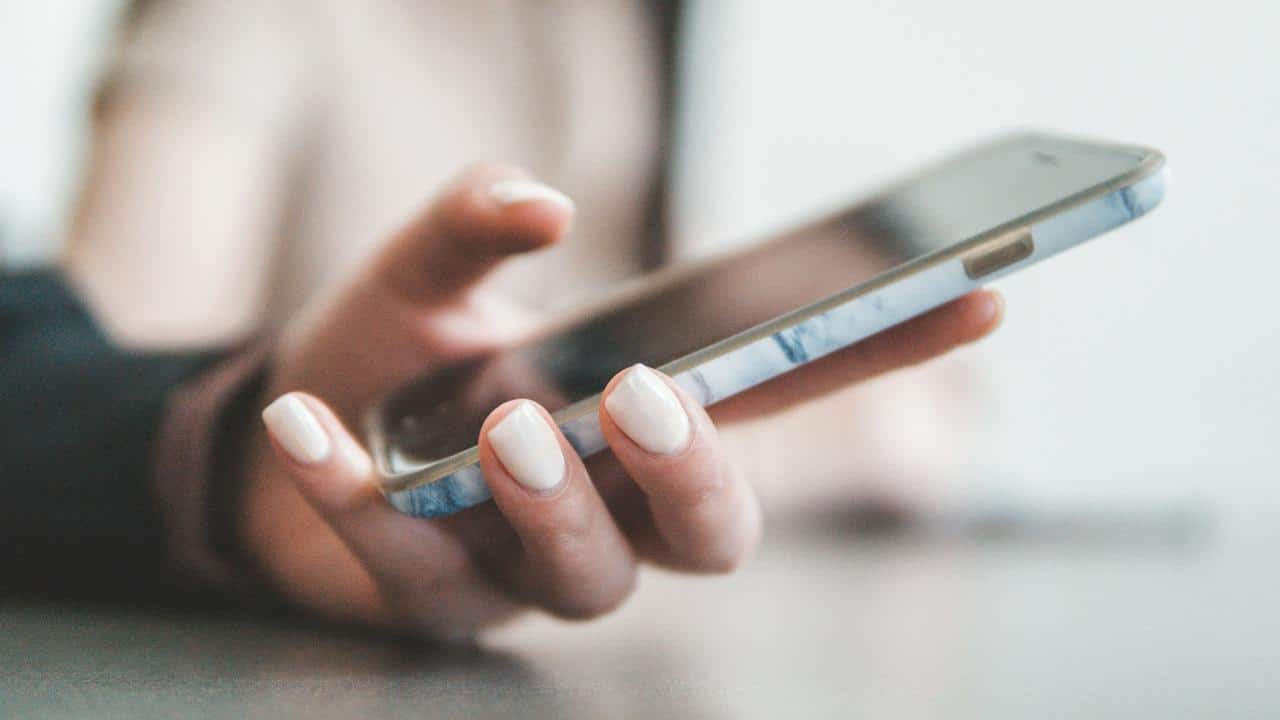 A close-up of a hand holding a smartphone with white polished nails.