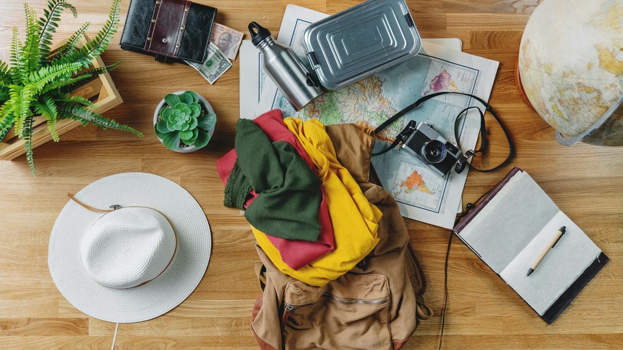 A flat lay of travel essentials, including clothes, a backpack, a map, a camera, a notebook, and a hat.