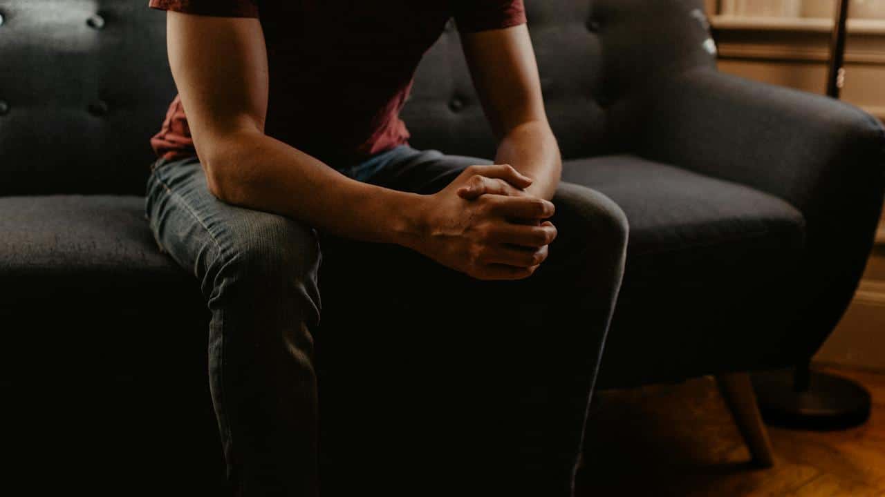 A man sitting on a couch with his hands clasped together.