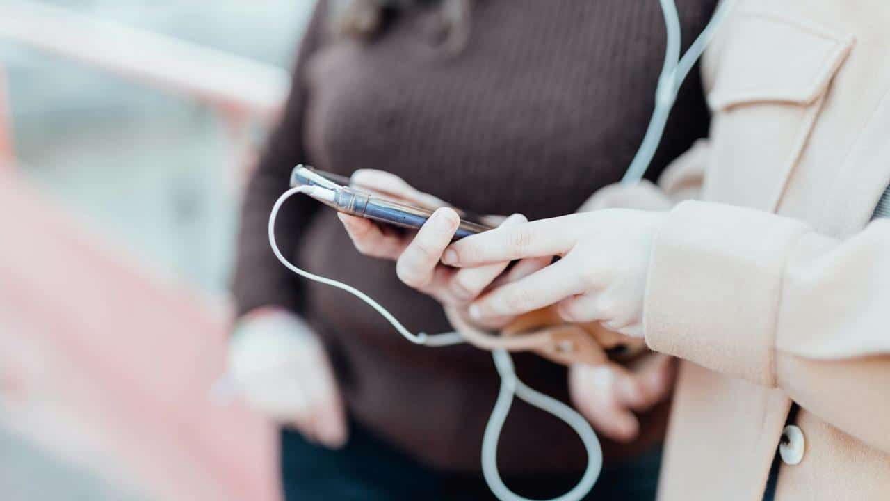 A close-up of two people holding a smartphone together with earphones plugged in.