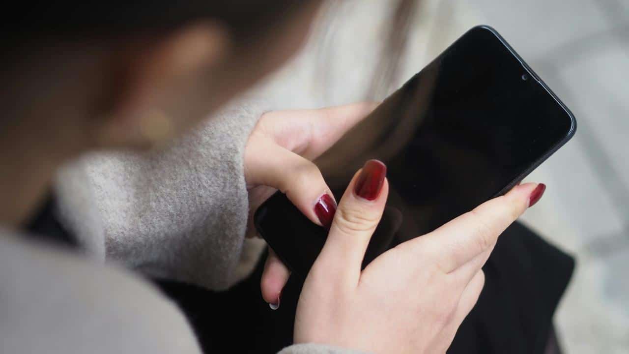 A close-up of a woman’s hands with red nails holding a smartphone.