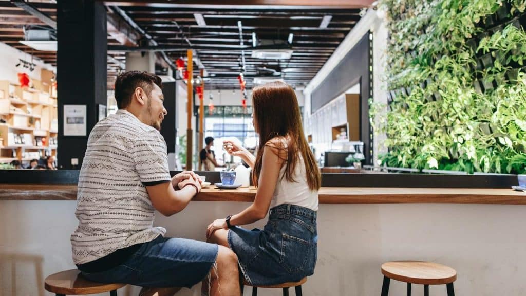 A man and woman sit at a café counter enjoying drinks and conversation.