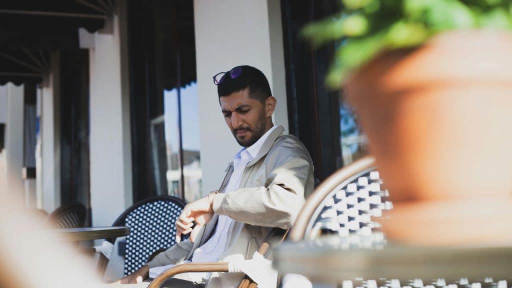 A man sitting at an outdoor café table while checking his watch.