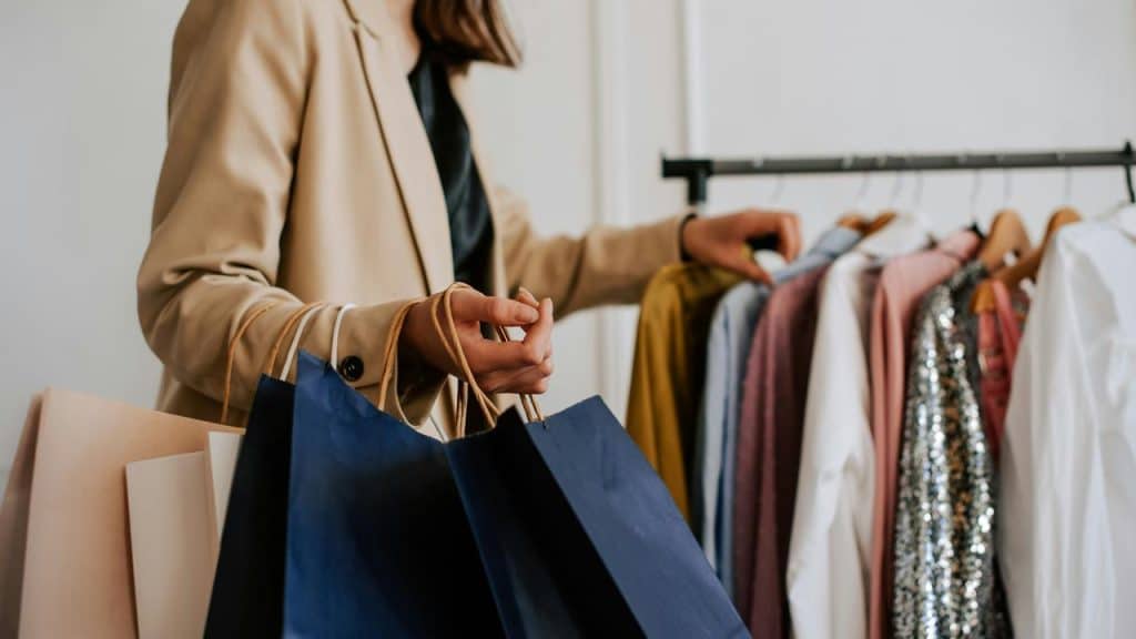 A woman holding shopping bags while browsing clothes on a rack.