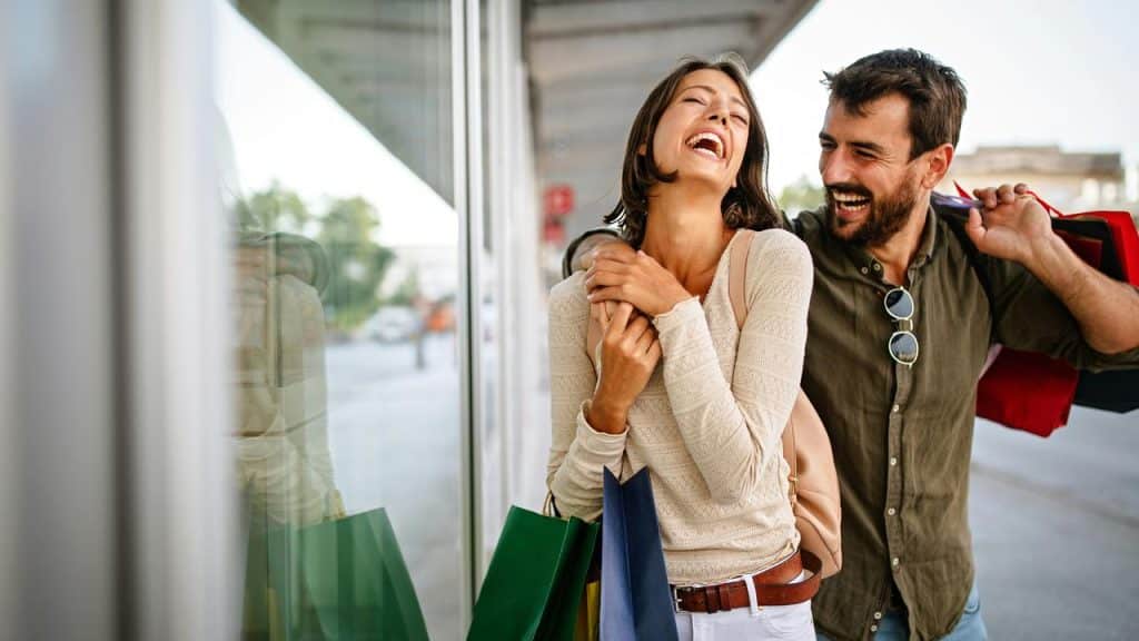 A happy couple laughing and carrying shopping bags outside a store.