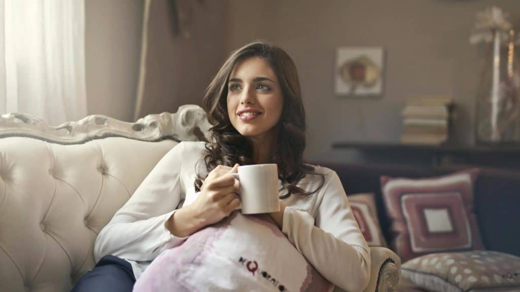 A woman sitting on a couch, smiling while holding a mug.