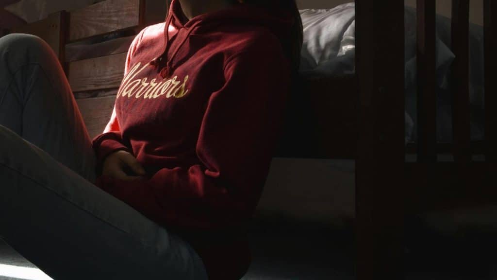 A person sitting on the floor in a red hoodie with "Warriors" written on it.