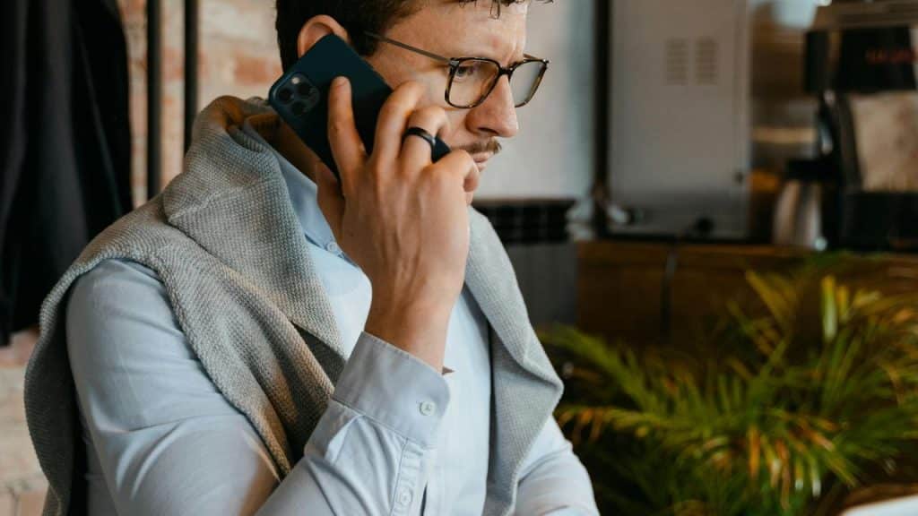 A man wearing glasses talking on a smartphone indoors.