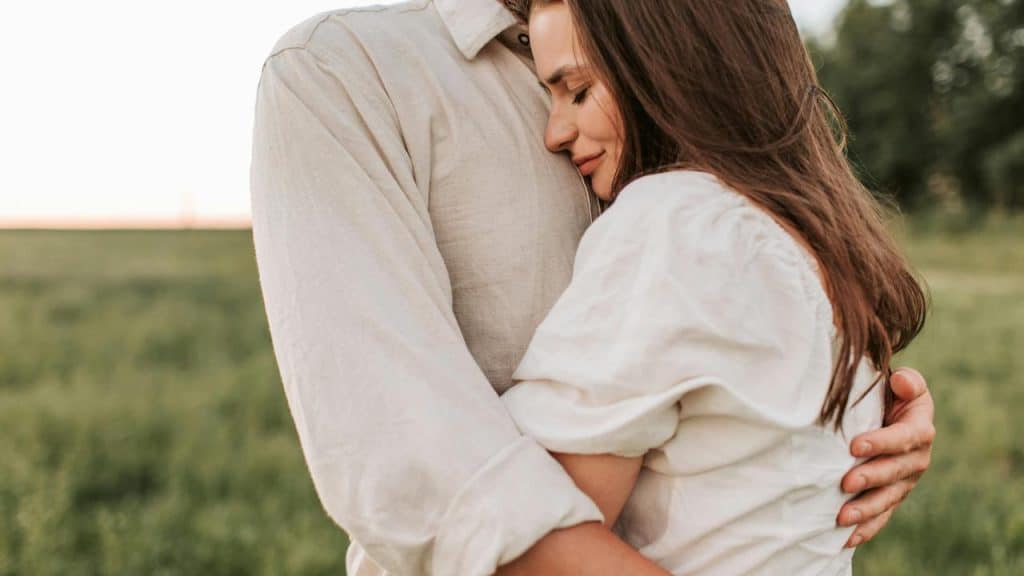 A woman hugging a man outdoors with a peaceful expression.