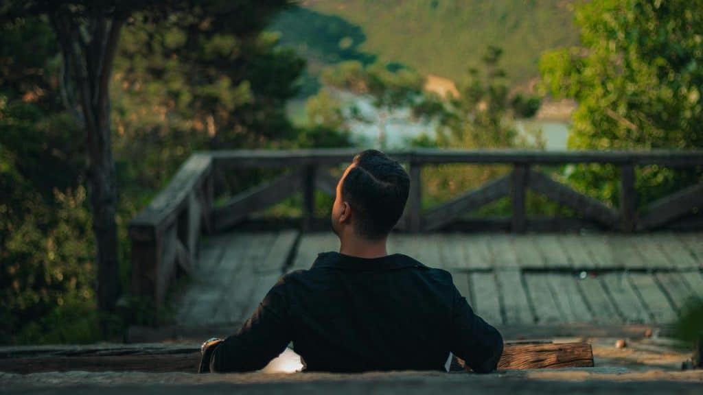 A man sitting on a wooden bench outdoors looking up at the sky.