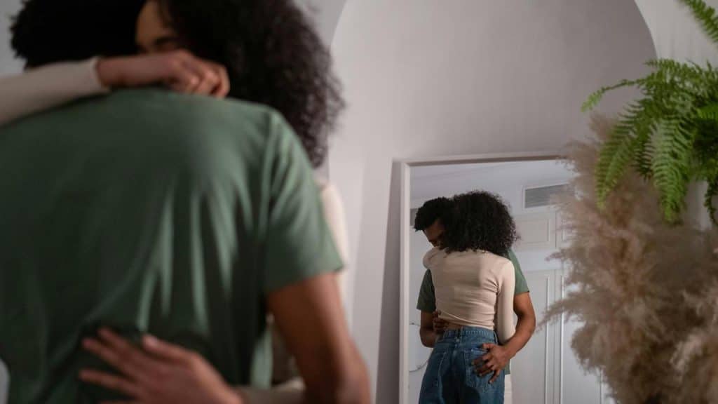 A couple hugging closely in front of a mirror indoors.